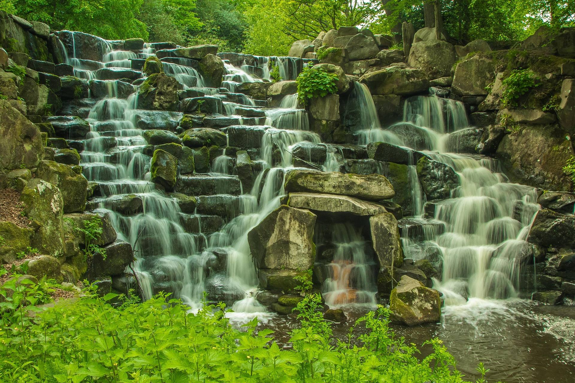 Water spilling in wide sheets over stacked stone ledges into a green forest pool