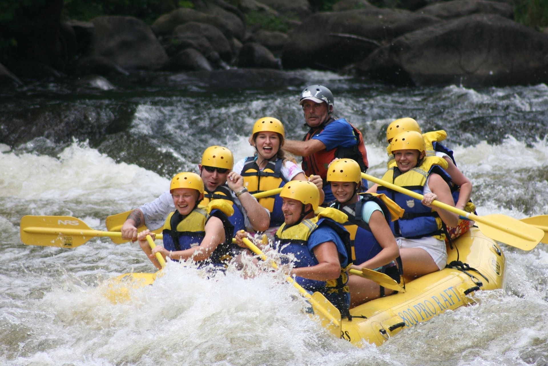 Family and friends paddling a yellow raft through whitewater rapids on a guided rafting trip