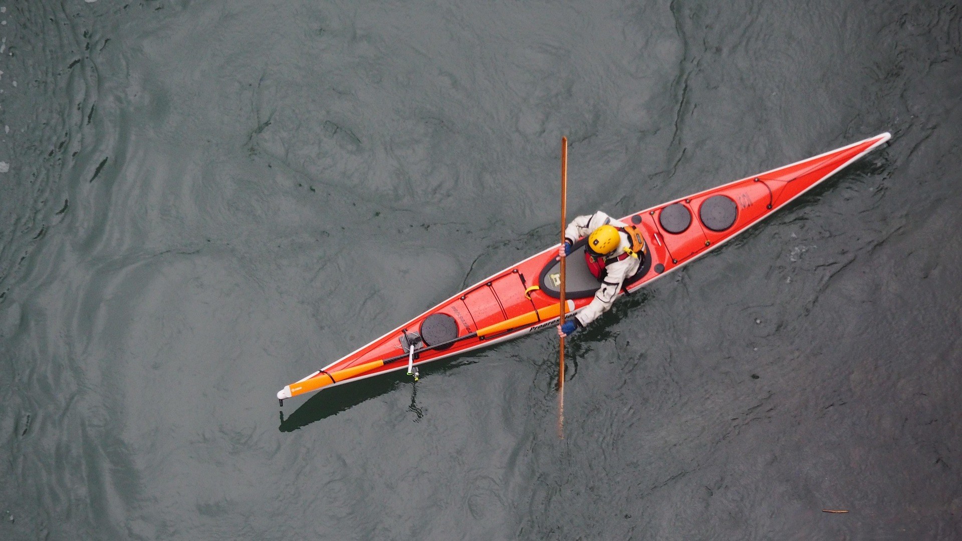 Overhead view of a paddler in a red sea kayak crossing calm dark water