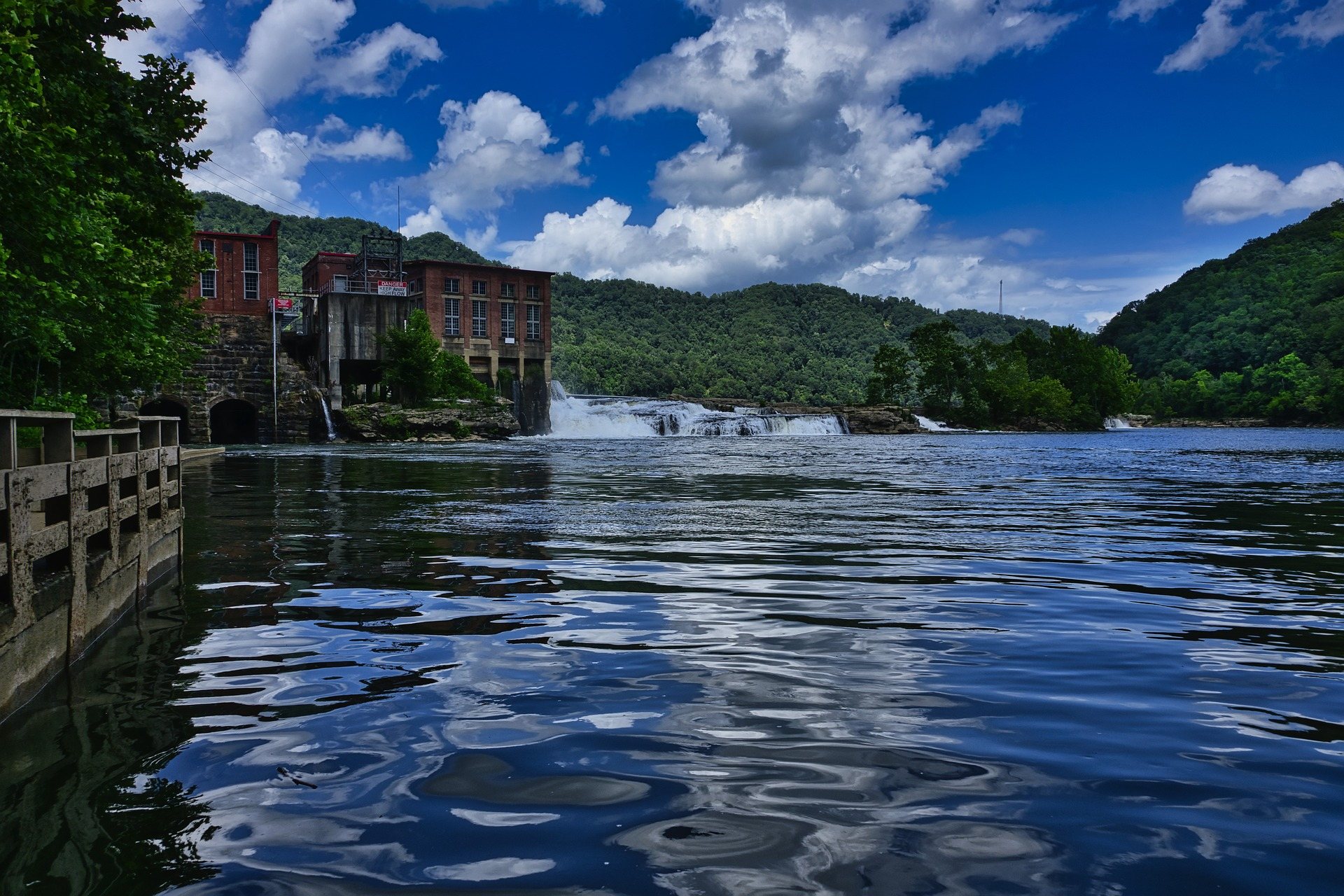 A low dam and brick hydroelectric plant on a broad West Virginia river, with wooded hills behind