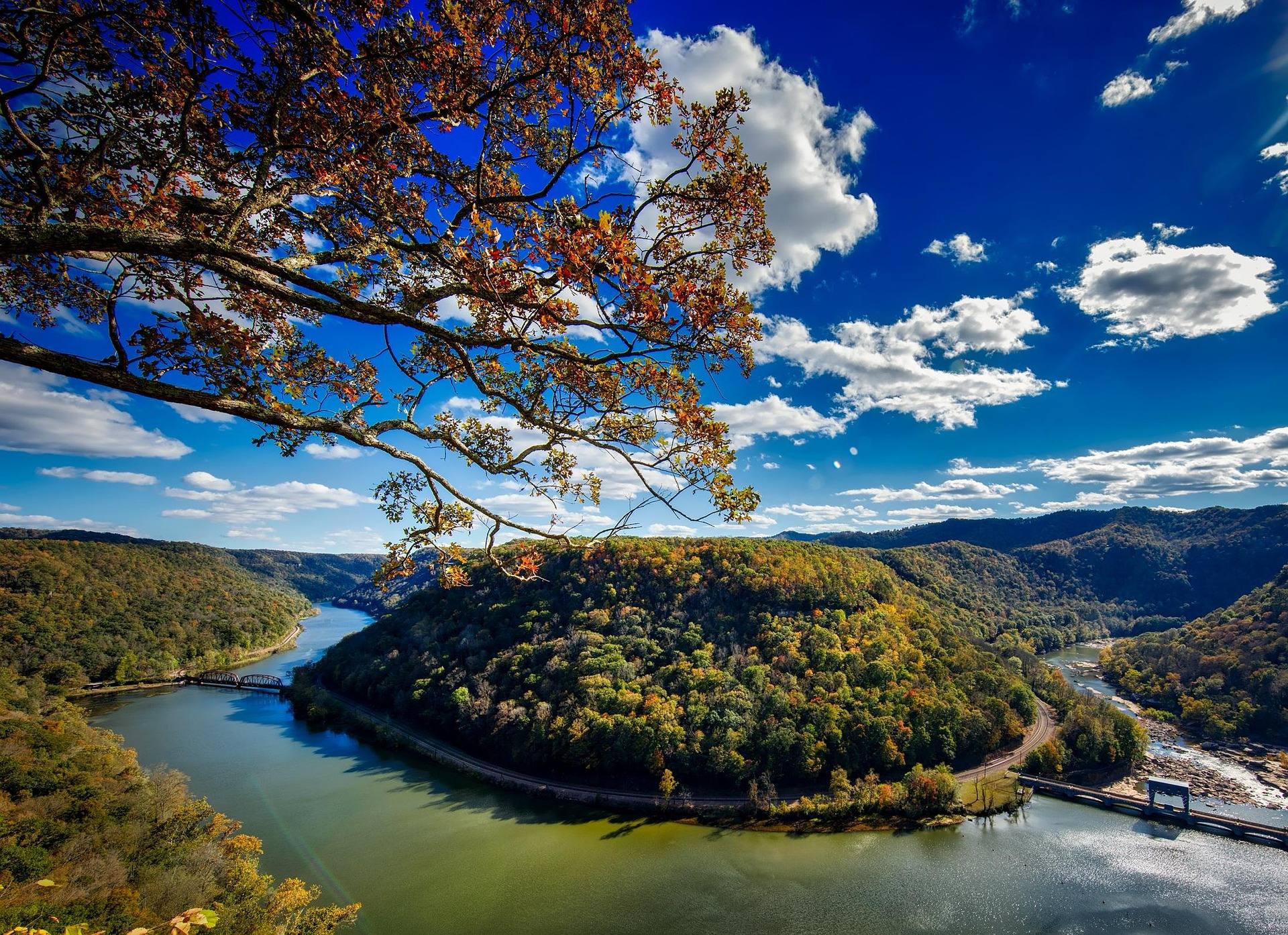 A river bending through a steep forested gorge in West Virginia under autumn foliage, with a road along the far bank