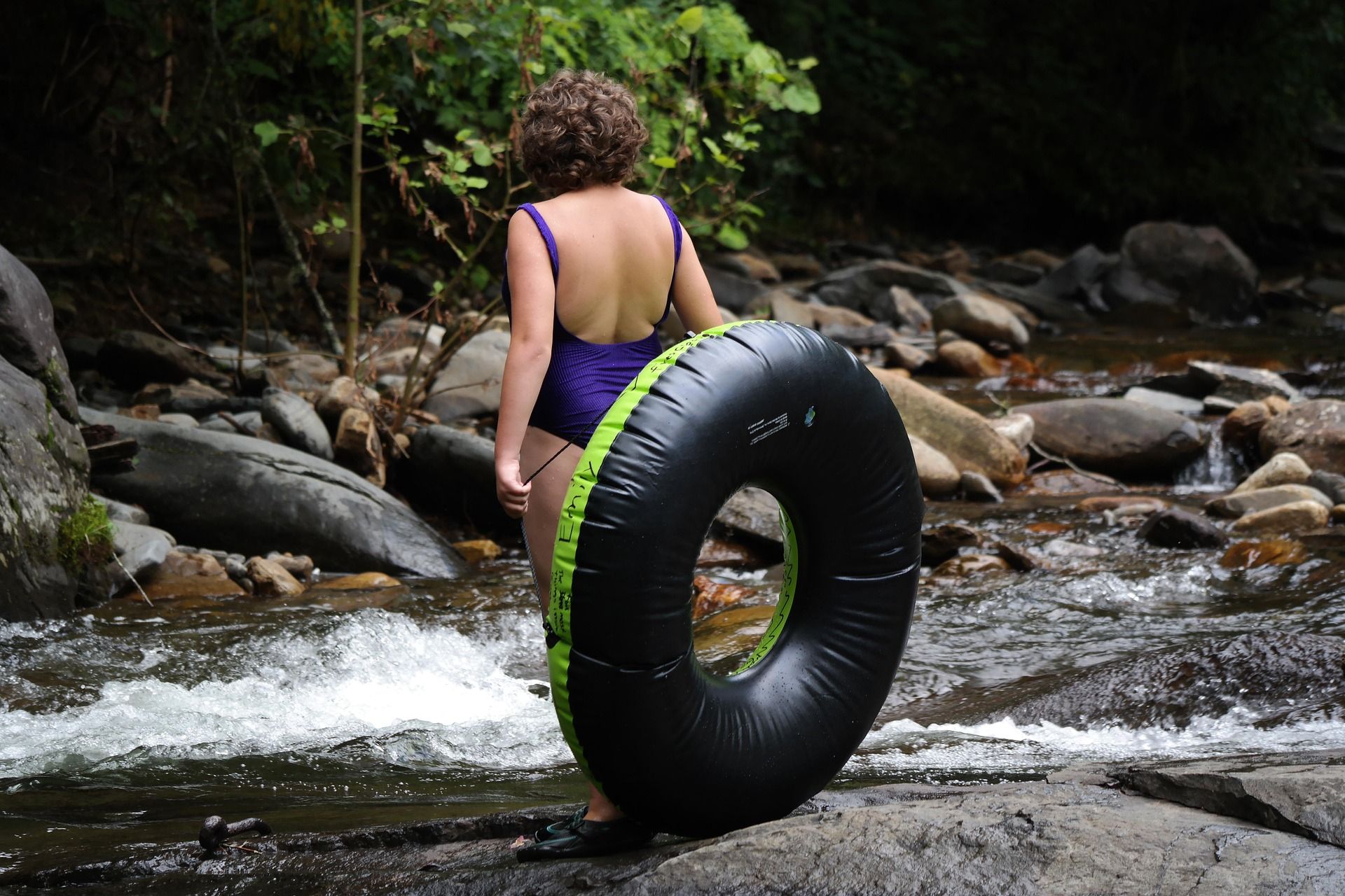 Woman carrying an inner tube into a rocky mountain creek on a summer river tubing trip