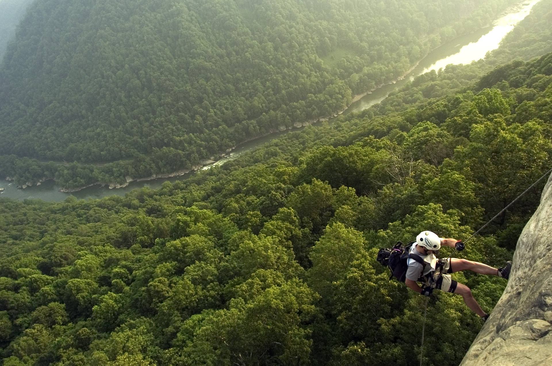 Rock climber on a sandstone cliff high above the forested New River Gorge in West Virginia