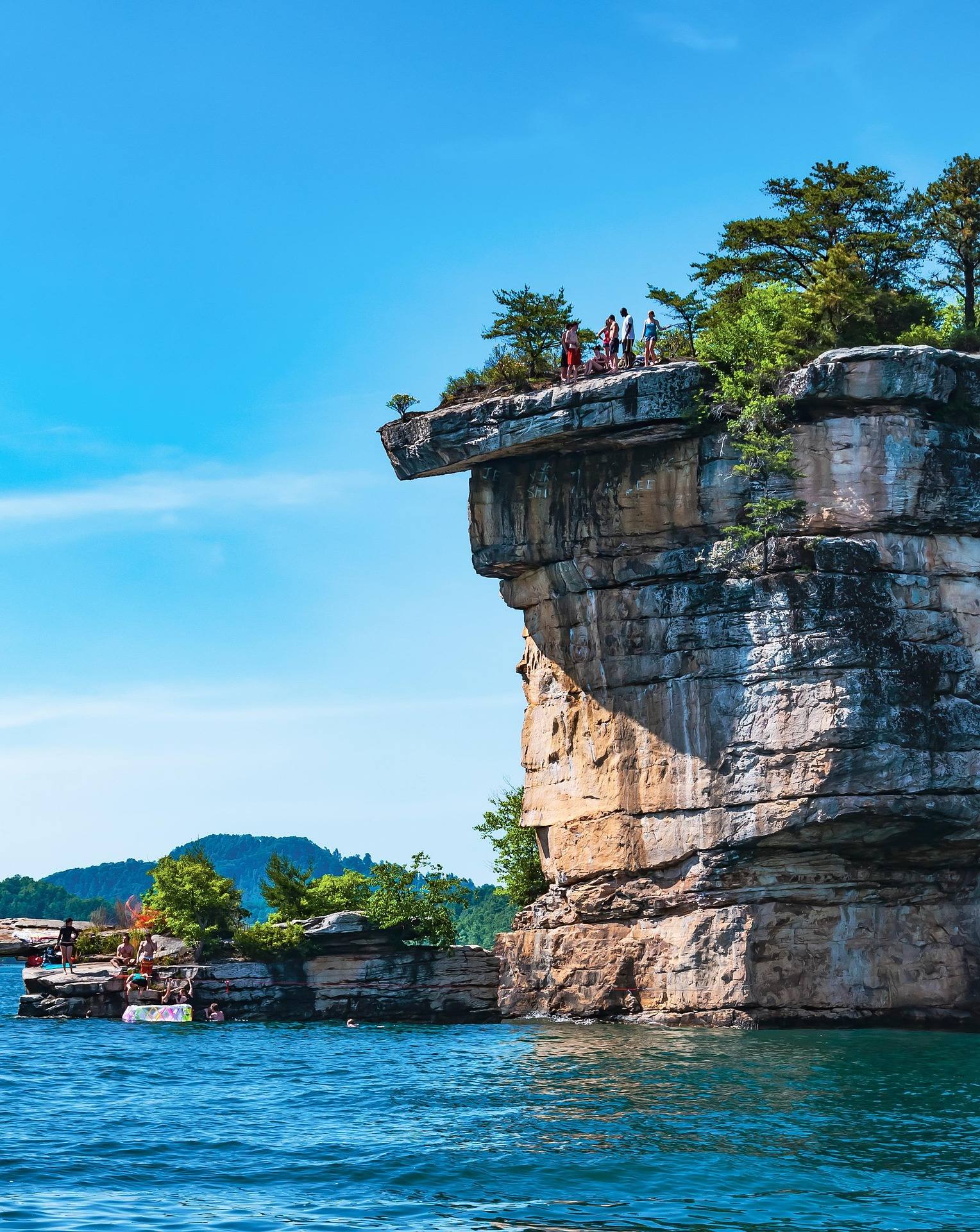 People standing atop an overhanging sandstone cliff above Summersville Lake with boats moored below, West Virginia