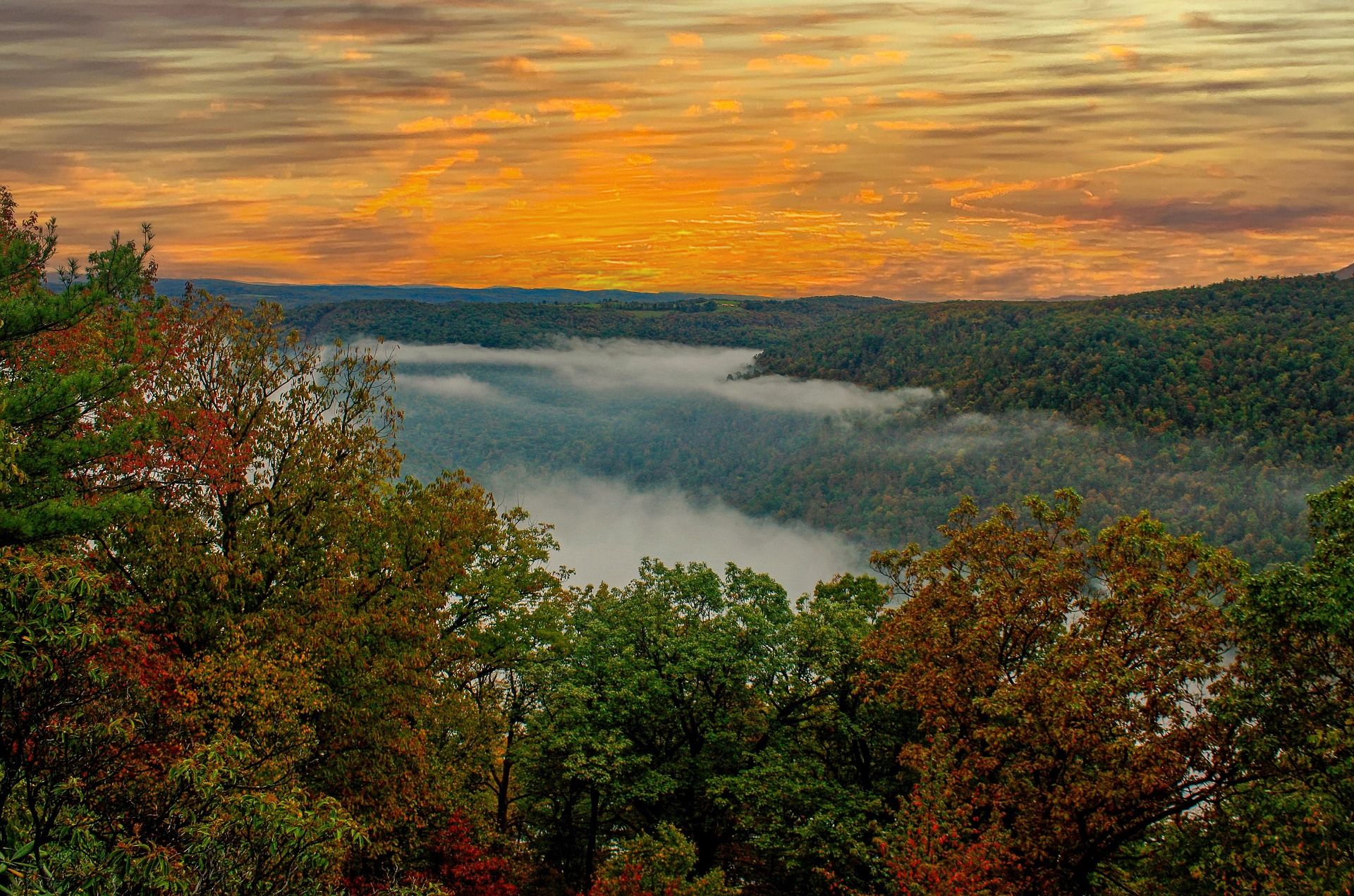 Sunrise burning orange over a fog-filled West Virginia river valley with autumn colour on the near ridge